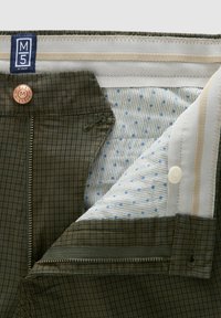 Grüne karierte Herrenhose mit Reißverschluss. Das Innenfutter zeigt ein hellblaues, gemustertes Futter und ein Kupferknopfdetail.