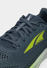 Κοντινή λήψη μπλε παπουτσιού Altra Escalante Racer με διχτυωτό επάνω μέρος, μπλε κορδόνια και λαμπερό κίτρινο λογότυπο στο πλάι.