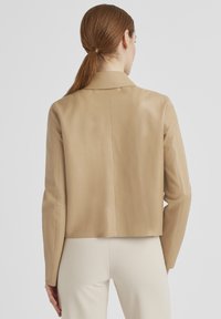 Tanfarbene Lederjacke mit verkürztem Schnitt, eingekerbtem Kragen und langen Ärmeln. Glatte Textur und einfache Nahtdetails an der Rückseite.