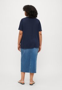 Navy blue short-sleeve top with a relaxed fit, paired with a denim midi skirt and flat sandals, viewed from the back.