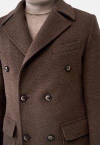 Brown double-breasted coat made of wool with wide lapels and black buttons; features a chest pocket and textured fabric.
