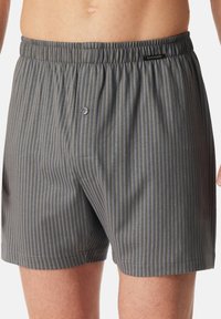 Boxers à rayures grises et bleues en tissu léger, avec une taille élastique et un détail de bouton à l'avant.
