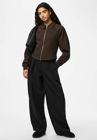 Veste marron courte avec fermeture éclair, associée à un pantalon noir à jambes larges. Sac texturé et chaussures noires à enfiler complètent la tenue.