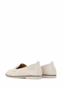 Paire de mocassins à enfiler en cuir blanc cassé avec semelles plates basses et une bande décorative sur le dessus, montrés de dos et de côté.