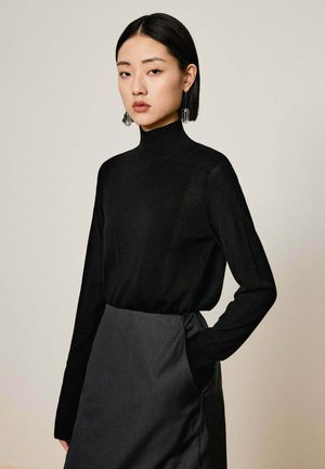 Schwarzer Rollkragenpullover mit langen Ärmeln, aus leichtem Stoff, kombiniert mit einem dunkelgrauen Rock, der eine Seitentasche aufweist.