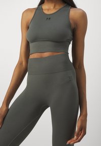 Tmavě zelený upnutý sportovní crop top a legíny s vysokým pasem s žebrovanou texturou, s malým logem na hrudi a na stehně.