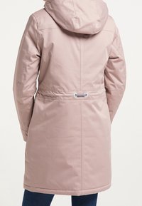 Ljusrosa vattentålig kappa med huva, dragsko i midjan och slät tyg. Längden når till mitten av låret och har ingen synlig hårdvara.