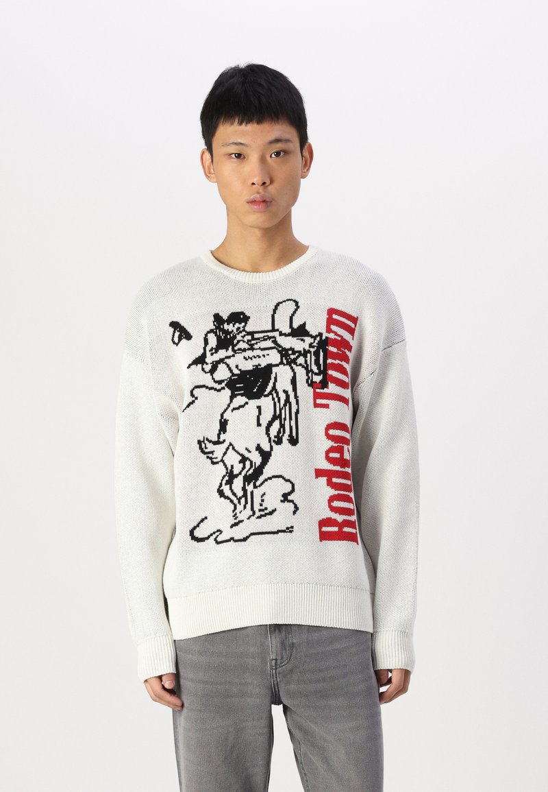 Witte gebreide trui met een grafische print van een cowboy die op een paard rijdt, voorzien van zwarte en rode accenten, ronde hals en geribde manchetten.