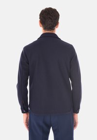 Giacca in misto lana blu navy con colletto, maniche lunghe, polsini con bottone e taglio dritto, caratterizzata da una texture liscia e da una leggera lucentezza.