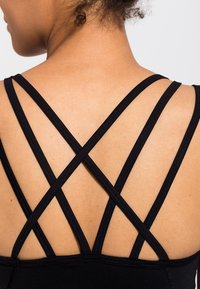 Svart sportstopp med flerkorsad design på baksidan, med korsade band och en slät yta. Utan utsmyckningar eller mönster.