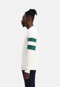 Sudadera blanca con rayas verdes en la manga izquierda, mangas largas, cuello redondo y un corte relajado. Textura de tela suave.