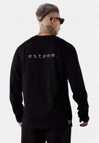 Schwarz langärmliges T-Shirt mit weißem Text "esteem." auf der Rückseite, aus weichem Stoff mit lockerer Passform und minimalistischem Design.