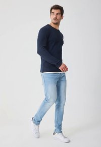 Tmavě modré tričko s dlouhým rukávem, světle modré džíny a bílé tenisky. Tričko má kulatý výstřih a džíny jsou s úzkým střihem.