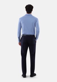 Hellblaues Langarmhemd mit klassischem Kragen, kombiniert mit dunkelblauen Hosen. Das Outfit hat eine taillierte Passform und dezente Knöpfe an den Ärmelbündchen.