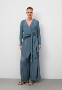 Niebieski zestaw z plisowanym materiałem, długimi rękawami, paskiem do związania i spodniami o szerokich nogawkach. Gładka tekstura i wzór w ukośne paski na całej powierzchni.