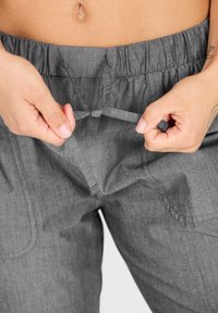 Harmaat kangashousut, joissa on joustava vyötärö ja säädettävä nyöri. Ominaisuuksiin kuuluvat sivutaskut ja sileä rakenne.