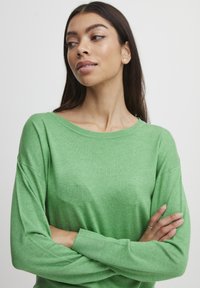 Vihreä kevyt neule, jossa on rento istuvuus, pyöreä kaula-aukko ja pitkät hihat. Kankaan pinta on sileä ja siinä on hienovarainen heather-kuvio.