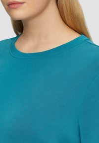 Türkisfarbener Baumwoll-T-Shirt mit rundem Ausschnitt und glatter Textur. Nahaufnahme, die die Schulternaht und die Details des Ausschnitts zeigt.