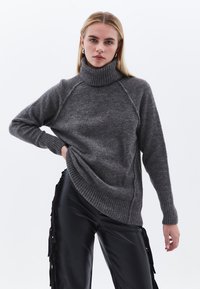 Maglione grigio a collo alto in materiale morbido e testurizzato, con polsi e orlo a coste. Presenta maniche raglan. Abbinato a pantaloni neri in finta pelle.