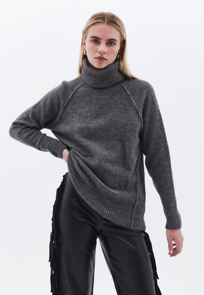 Maglione grigio a collo alto in materiale morbido e testurizzato, con polsi e orlo a coste. Presenta maniche raglan. Abbinato a pantaloni neri in finta pelle.