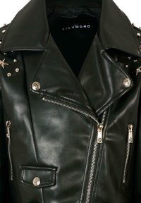 Giubbotto in pelle nera con ampio colletto, borchie argentate sulle spalle, tasche con zip e chiusura frontale diagonale con zip. Texture liscia.