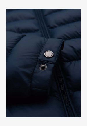 Donkerblauwe gewatteerde jasvoering met een gestructureerde afwerking, voorzien van een zilveren drukknoop en ritsdetails voor een veilige sluiting.
