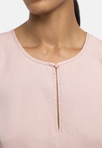 Różowa bluzka z okrągłym dekoltem, pionowym rozcięciem z małym detalem guzikowym oraz gładką, miękką teksturą.