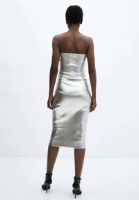 Robe métallisée argent sans bretelles, silhouette ajustée, ourlet à mi-genoux, texture lisse, portée avec des sandales à talons hauts à brides noires.