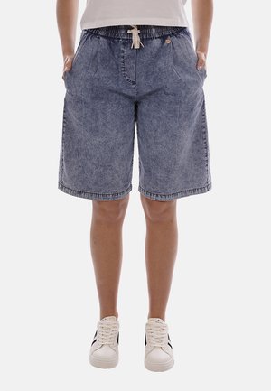 Persona che indossa pantaloncini di jeans blu sbiadito fino al ginocchio con cintura elastica e coulisse, abbinati a scarpe da ginnastica bianche.