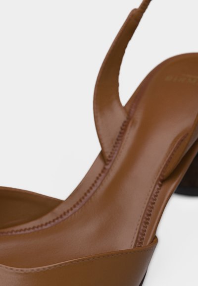 Καφέ δερμάτινο παπούτσι slingback με στρογγυλεμένη μύτη και χαμηλό τακούνι block, με εμφανείς ραφές κατά μήκος των άκρων.