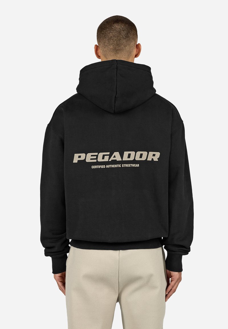 Juoda su gobtuvu džemperis su dideliu "PEGADOR" logotipu smėlio spalvos ir užrašu "CERTIFIED AUTHENTIC STREETWEAR" ant nugaros. Giliai apdirbti rankogaliai ir apatinė kraštinė.