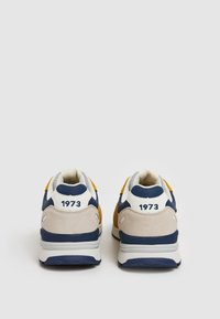 Sneakers con un mix di materiali blu navy, giallo e beige. Presentano una tomaia in suede morbido, inserti in rete e un prominente "1973" sul tallone.