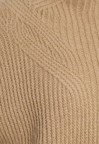 Beżowa dziana tkanina o prążkowanej fakturze i diagonalnym wzorze. Włókna wyglądają na miękkie i grube, co zwiększa ciepło i komfort.