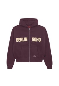 Bordó zipzáras kapucnis pulóver, amelyen a "BERLIN" és a "SOHO" krémszínű bolyhos betűkkel szerepel; elülső zsebbel és húzózsinórral ellátott kapucnival.