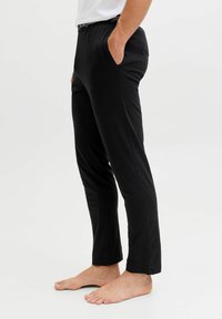 Černé kalhoty s tapered střihem, vyrobené z měkké tkaniny. Mají boční kapsy a elastický pas s logem.