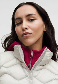 Jasnoszara pikowana kurtka z wysokim kołnierzem, z bordową warstwą wewnętrzną i zamkiem błyskawicznym. Gładka faktura z pikowanymi akcentami.