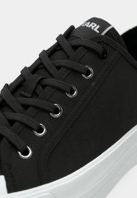 Μαύρα πάνινα παπούτσια με υφή ύφανσης, ασημένιες τρύπες κορδονιών και μαύρα κορδόνια. Διαθέτουν λευκή σόλα από καουτσούκ και ένα λογότυπο στη γλώσσα.