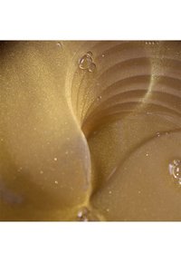 Un liquide doré avec un léger éclat, une texture lisse, et la lumière se reflétant sur des surfaces courbes ; présente de petites gouttes d'eau.