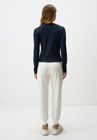 Marineblaues langärmeliges Oberteil mit taillierter Passform, kombiniert mit weißen Jogginghosen mit elastischen Bündchen und einer weichen Textur. Bequeme Schuhe sind enthalten.