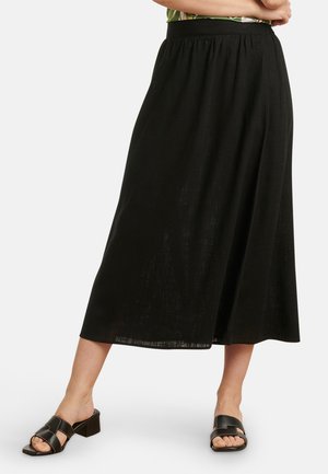 Schwarzer Midirock aus leichtem Stoff mit gerafftem Taillenbund und fließender Silhouette. Kombiniert mit schwarzen Blockabsatzsandalen.
