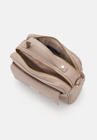 Beżowa skórzana torebka o teksturowanym wykończeniu, z podwójnymi zamkami błyskawicznymi, złotymi akcentami i małą metką wewnątrz. Kompaktowy, prostokątny kształt.