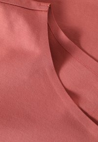 Puuvillakangas hillityssä korallinvärissä, jossa on sileä pinta, pyöreä kaula-aukko ja siisti ompelu reunoilla.