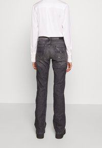 Dark gray denim jeans with a slim fit, featuring two back pockets and subtle distressing. Paired with a white long-sleeve shirt.