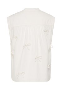 Blouse blanche sans manches avec tissu froncé et petits nœuds décoratifs éparpillés dans le dos.