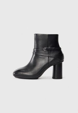 Black leather ankle boot with a rounded toe and a thick block heel. Features a decorative strap with a buckle accent. Smooth texture.