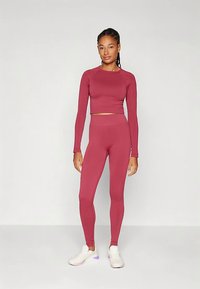 Bordo spalvos sportinis rinkinys, kuriame yra ilgomis rankovėmis trumpa palaidinė ir aukšto liemens leginsai, pagaminti iš lygaus, tamprios medžiagos; derinamas su baltais sportbačiais.