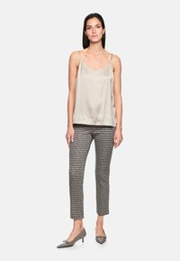 Satin, light beige camisole with thin straps, paired with black and white patterned trousers and gray kitten-heeled shoes.