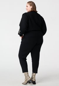 Zwarte korte trui met lange mouwen en bloemrijke borduursels op de manchetten, gecombineerd met zwarte aansluitende broek en beige enkellaarsjes met slangenprint.