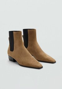 Botines de ante marrón hasta el tobillo con punta afilada, que presentan paneles laterales elásticos negros, tacón bajo y una textura suave.
