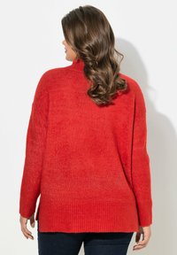 Roter Strickpullover mit hohem Kragen, überschnittenen Schultern und seitlichen Schlitzen am Saum. Weicher Stoff mit gerippten Bündchen und Saum.